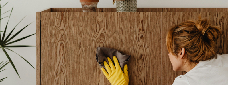 woman cleaning wood cabinets with gloved hand and microfiber cloth