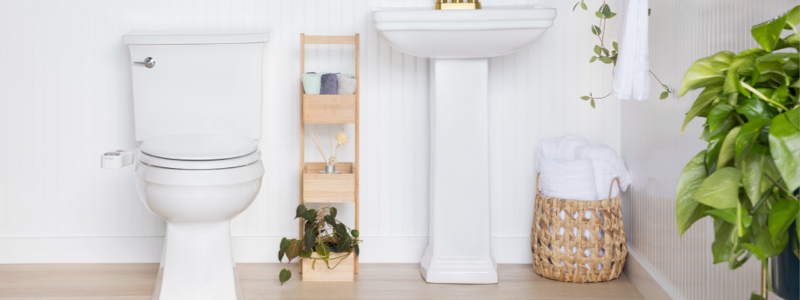 Brondell bidet attachment installed on standard toilet in a white bathroom with wooden storage caddy and plant accent